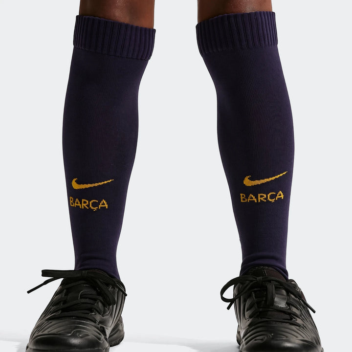 Close-up of a child's legs wearing dark blue Nike FC Barcelona soccer socks with gold logo and black soccer shoes.