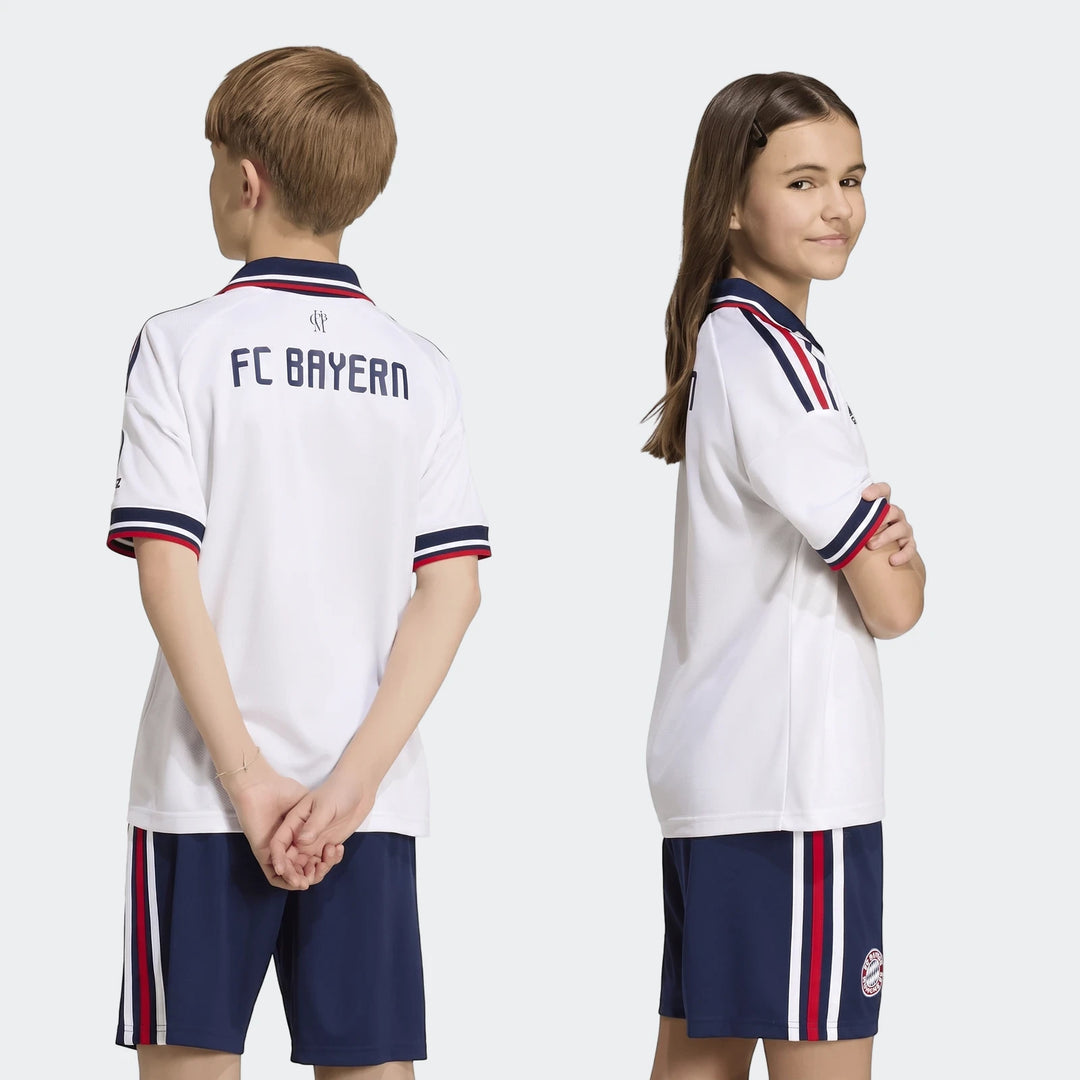 Two children modeling the Fc Bayern 26/27 Away Jersey for kids, featuring a white shirt with navy and red accents, paired