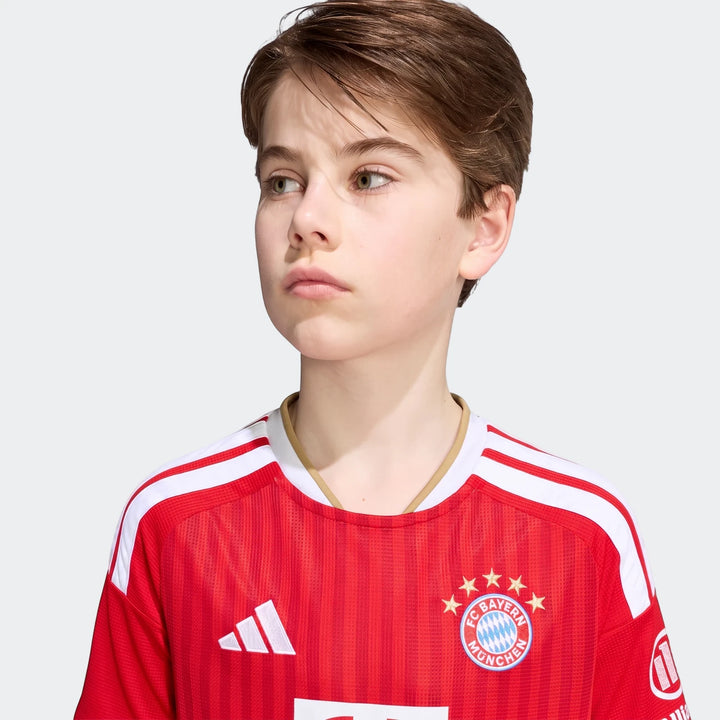 Young boy wearing a red Adidas FC Bayern 26/27 Home Kids Jersey with white stripes and team crest, viewed from the chest up.