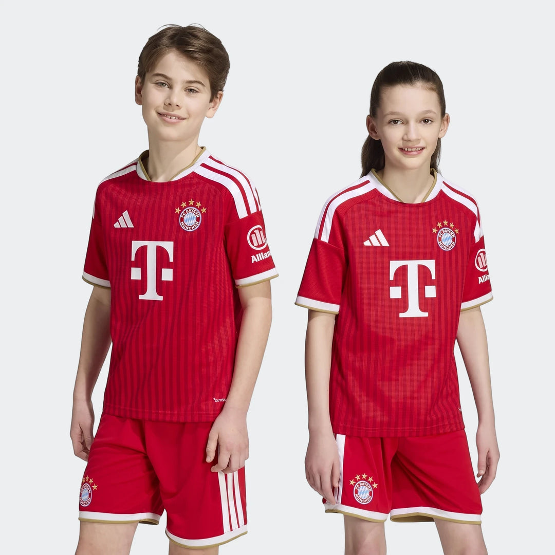Two children model the red Fc Bayern 26/27 Home Jersey Kids kit, featuring the club crest, sponsor logos, and white stripes.
