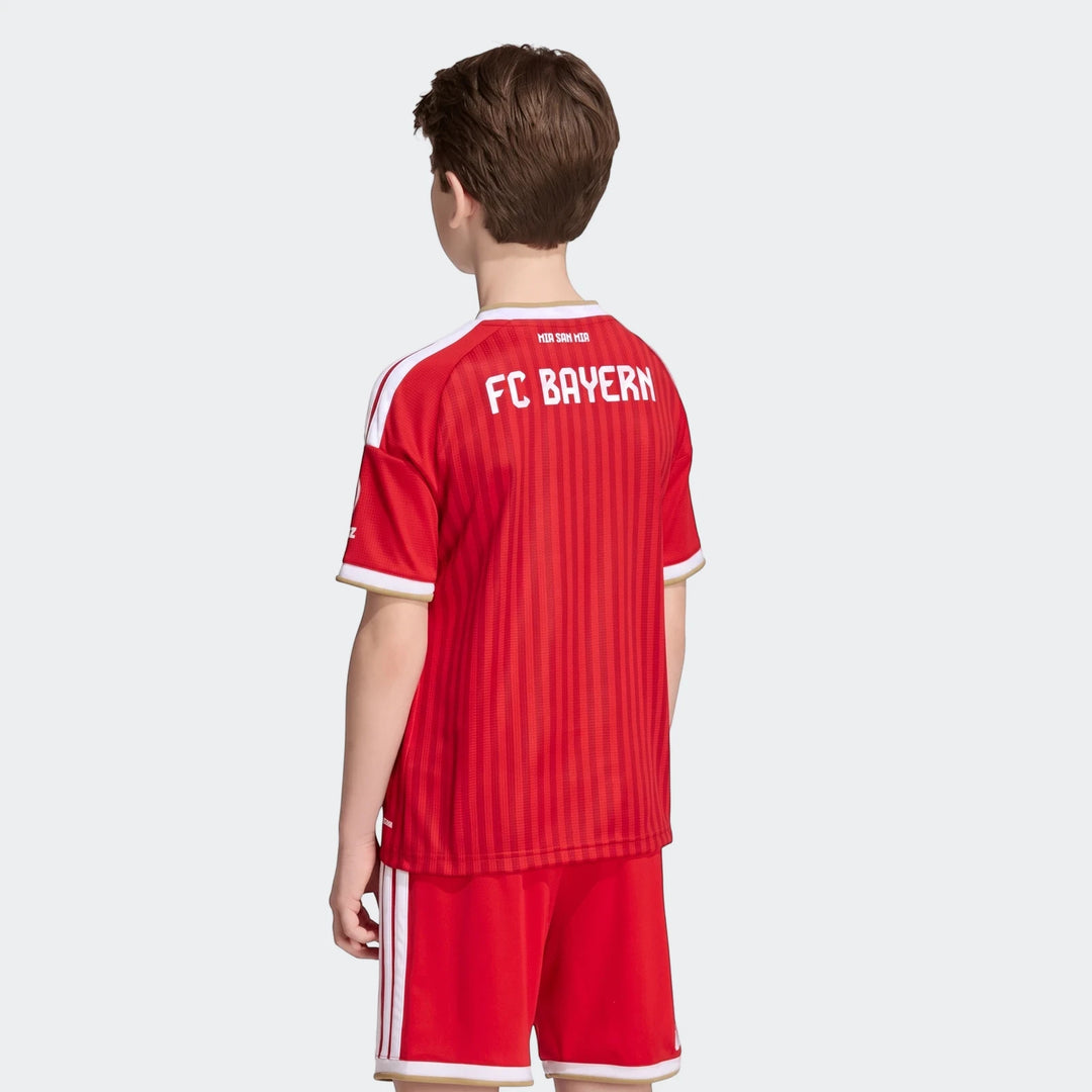 Back view of a young boy wearing a red Adidas FC Bayern 26/27 Home Jersey Kids and matching shorts with white stripes and