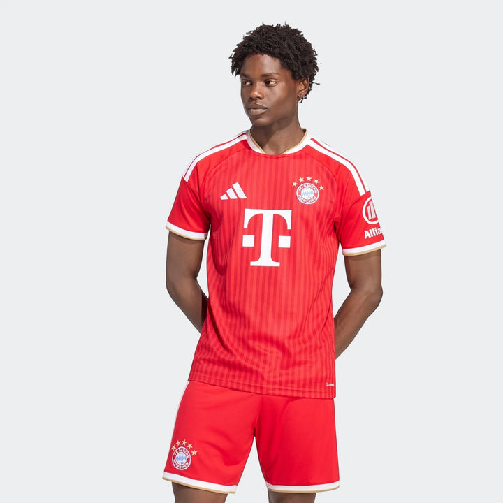 Male model in red Adidas FC Bayern 26/27 Home Jersey and matching shorts, front view.