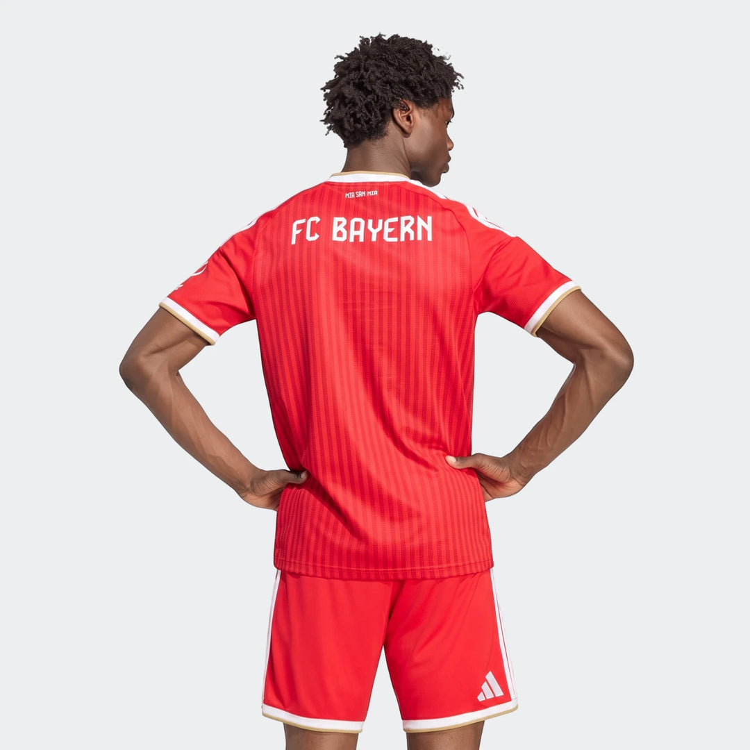 Men's red Fc Bayern 26/27 Home Jersey and matching shorts, seen from the back on a model with hands on hips.