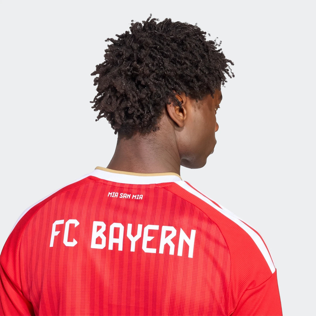 Back view of a person wearing the red Fc Bayern 26/27 Home Jersey with white "MIA SAN MIA" and "FC BAYERN" text on the back.