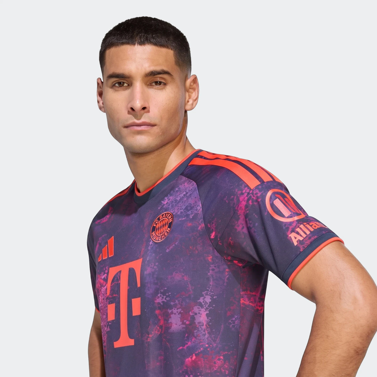 Male model wearing a purple and red patterned Fc Bayern 26/27 Third Jersey, showcasing the team and sponsor logos.