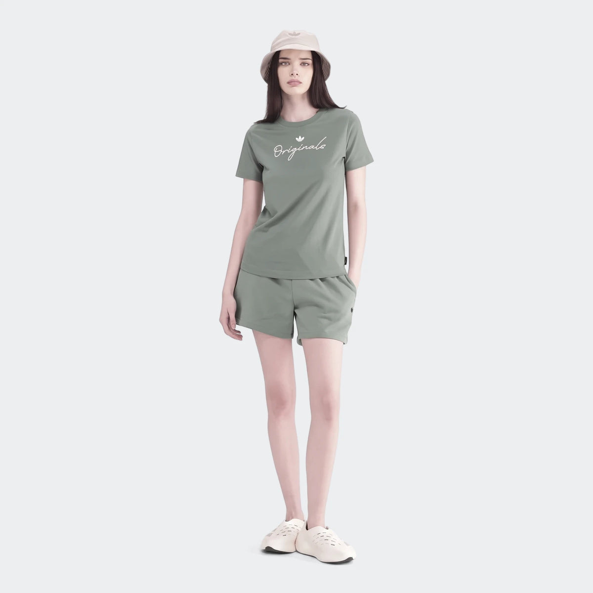 Female model in a green short-sleeve 'Originals' t-shirt, matching shorts, and a beige bucket hat, on a white background.