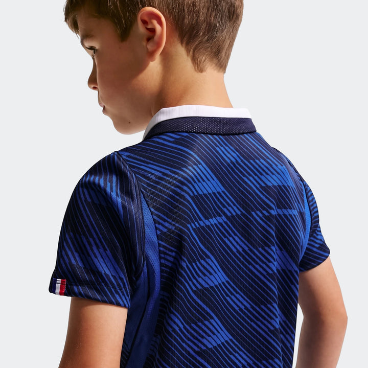 Young boy from behind wearing a blue patterned Fff 2026 Stadium Home Little Kids' Nike Soccer Replica polo shirt with a