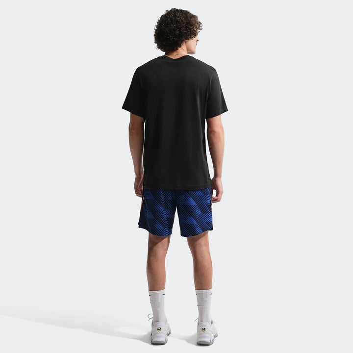 Man from behind wearing a black Nike soccer t-shirt and blue patterned shorts, white socks, and sneakers.