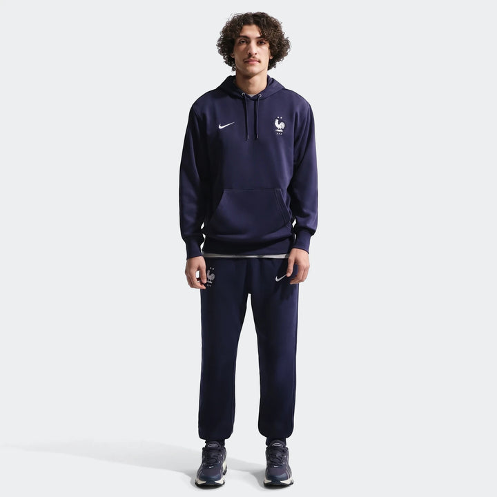 Full body shot of a man wearing a navy blue Fff Club Nike Soccer French Terry Pullover Hoodie and matching sweatpants.