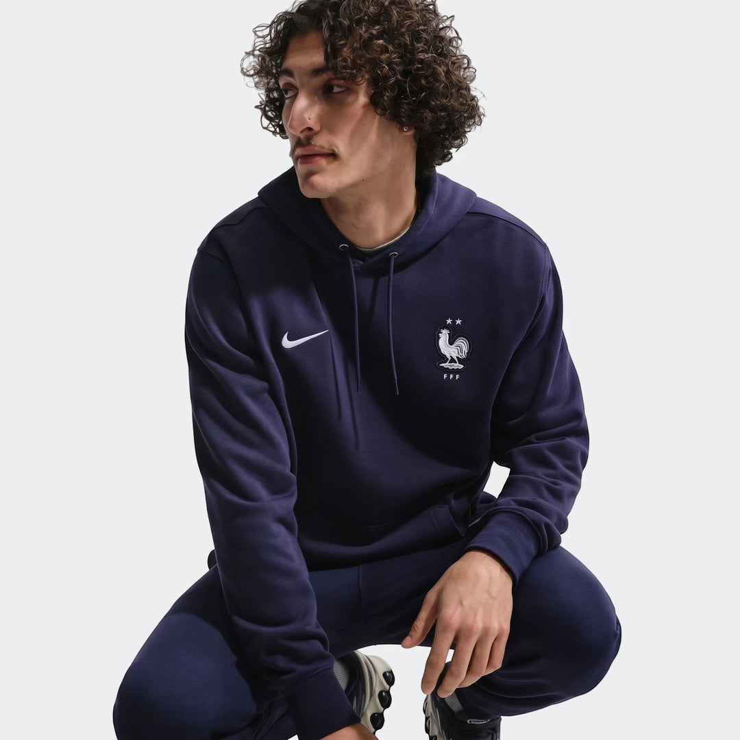 Men's Nike FFF Club French Terry Pullover Hoodie in navy blue, modeled in a squatting pose.
