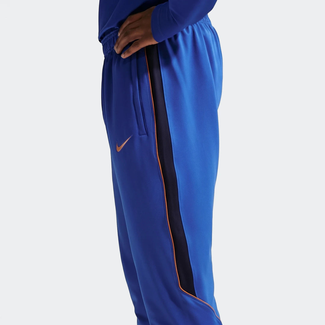 Men's FFF Strike Nike Dri-Fit soccer knit pants in royal blue with side stripes, worn by a model.