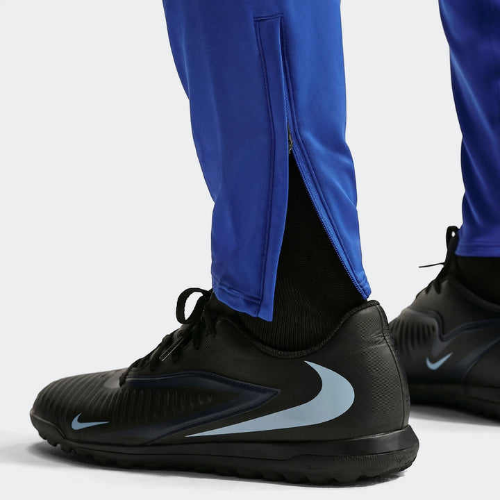 Close-up of a person wearing Fff Strike blue Men's Nike Dri-Fit soccer knit pants and black Nike soccer shoes.