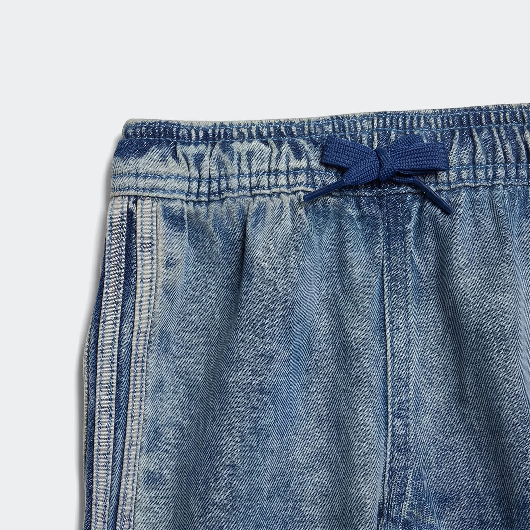 Close-up of blue Firebird denim track pants featuring an elastic waistband with a blue drawstring tied in a bow and white
