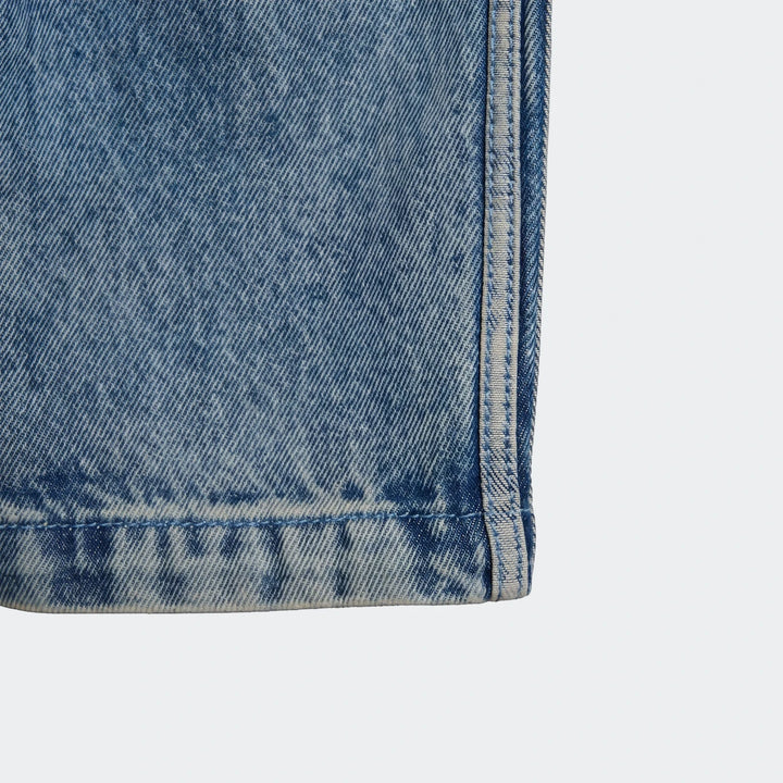 Close-up of blue faded Firebird Denim Track Pants fabric showing vertical seam and horizontal hem detail.