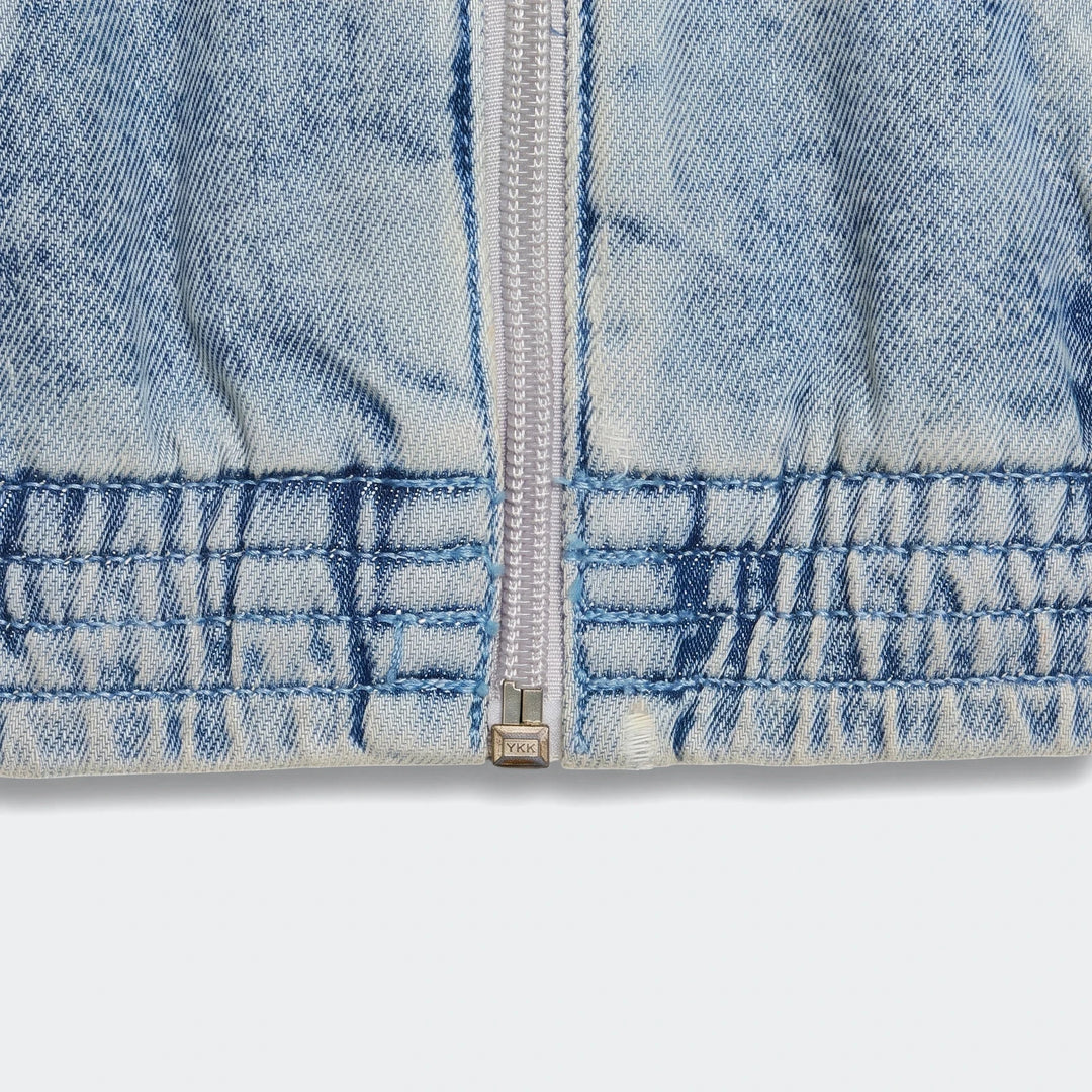 Close-up of a light blue acid wash Firebird Denim Track Top, featuring a silver front zipper and elasticated hem details.