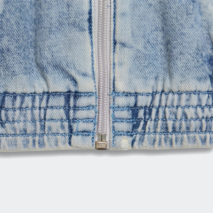 Close-up of a light blue acid wash Firebird Denim Track Top, featuring a silver front zipper and elasticated hem details.