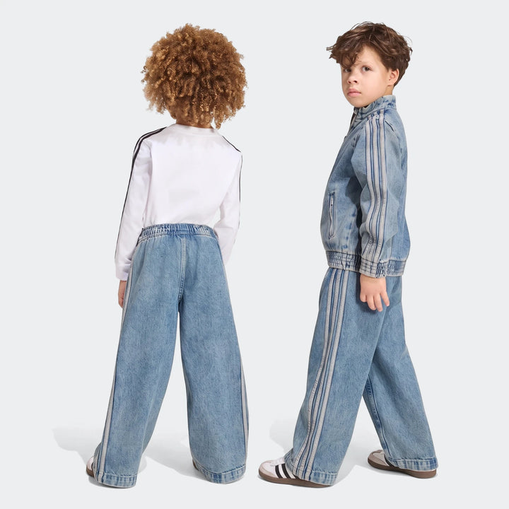 Two children wearing blue Firebird Loose Denim Track Pants and matching jackets with white stripes, standing.