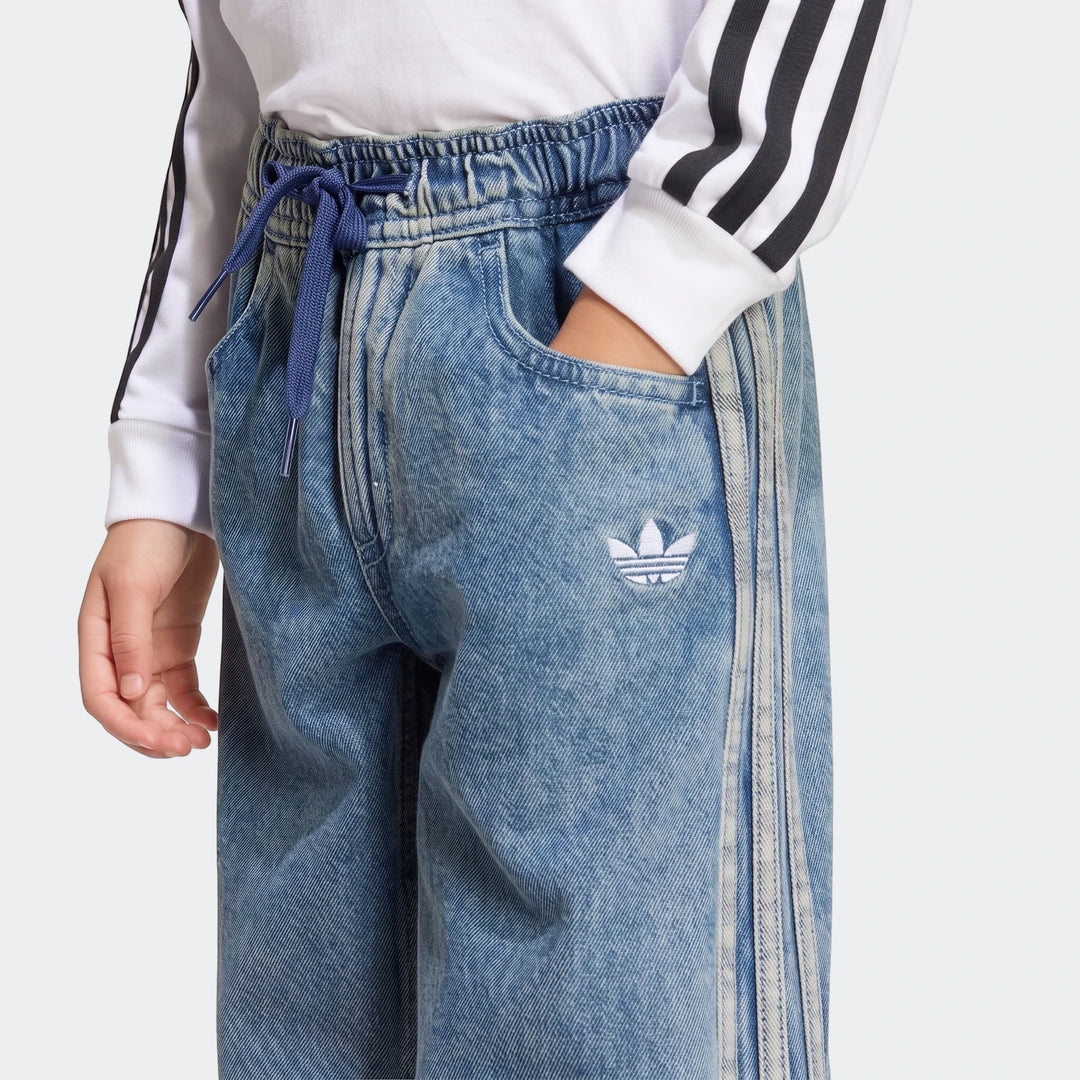 Close-up of light blue Firebird Loose Denim Track Pants with Adidas Trefoil logo and side stripes, worn by a person with