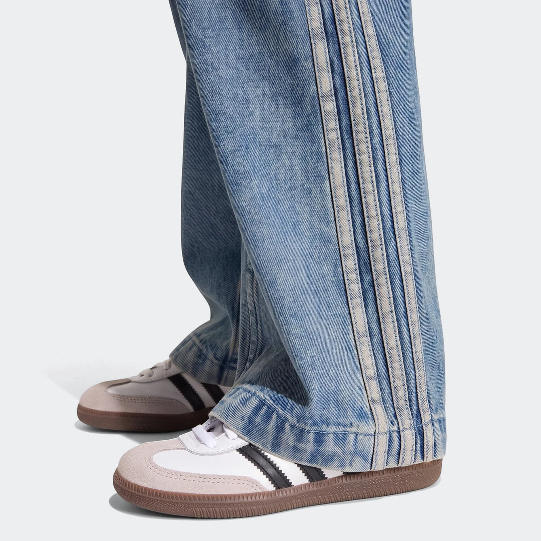 Close-up of light blue Firebird loose denim track pants featuring three white stripes, paired with white and gray sneakers.