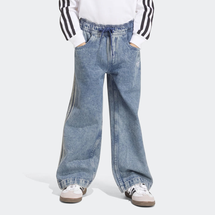 Youth's blue denim Firebird Loose Track Pants with white side stripes, shown worn by a person from waist to feet.