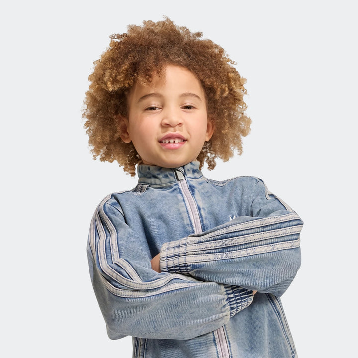 Young child wearing an Adidas Firebird Loose Denim Track Top with white stripes, captured in a studio portrait.