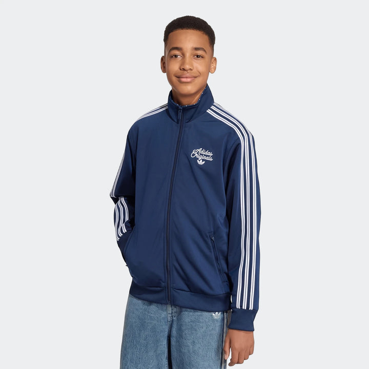 Young boy wearing a navy blue Adidas Originals Firebird Loose Reversible Tracktop with white three stripes on the sleeves.