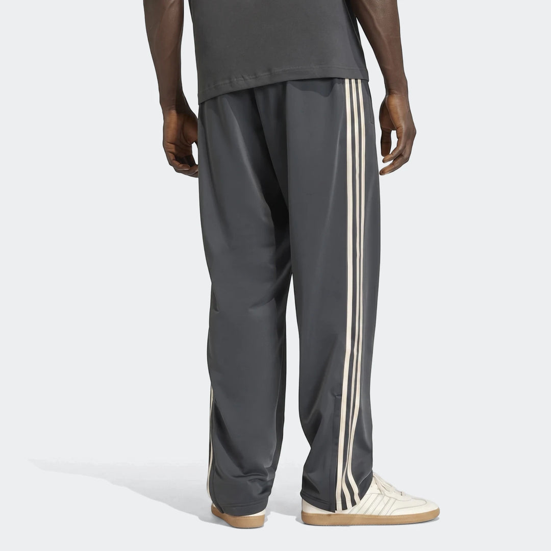 Dark gray Adidas Firebird Track Pants featuring three light stripes down the side, worn by a model from the back view.