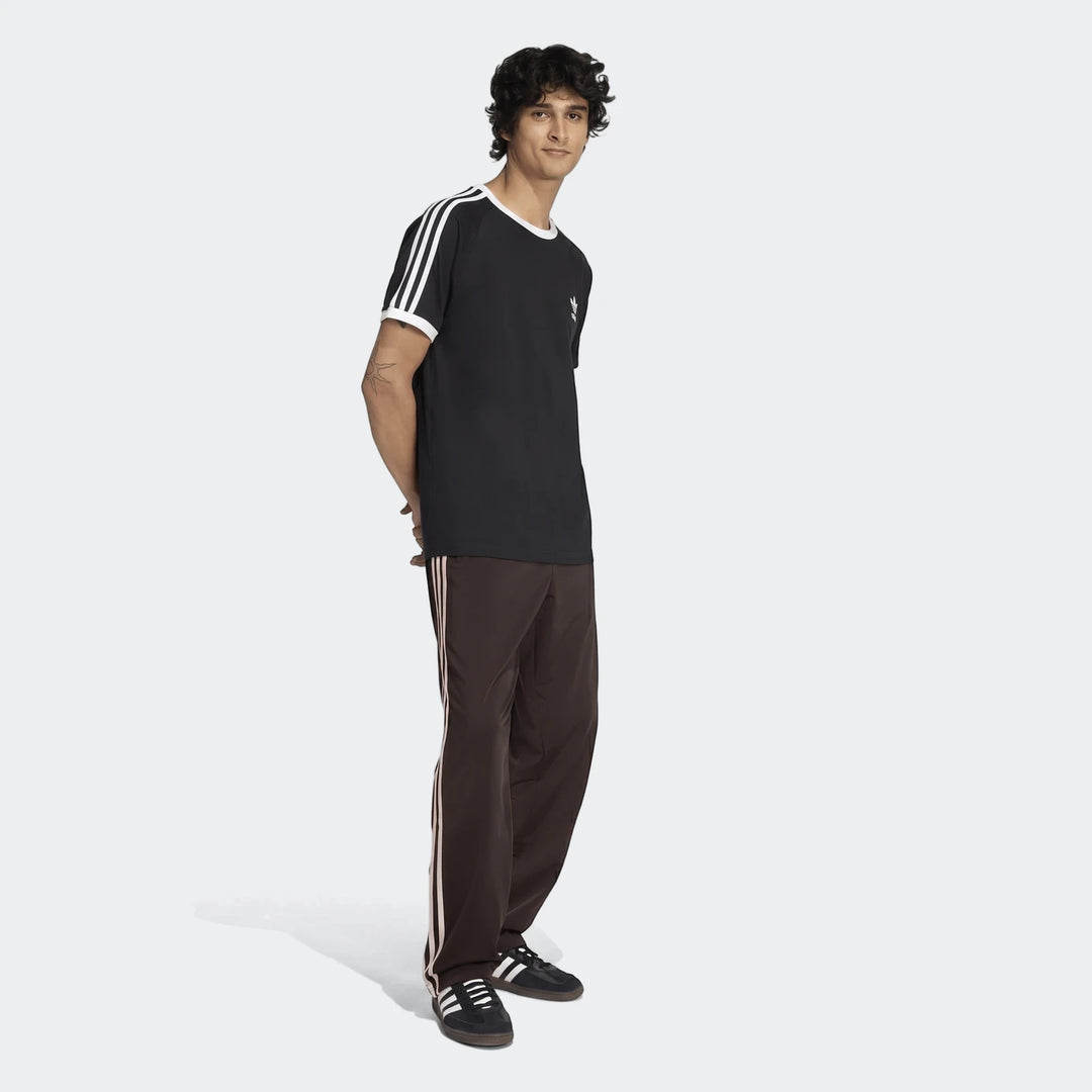 Male model wearing black Adidas t-shirt, brown Firebird track pants with pinkish stripes, and black sneakers.