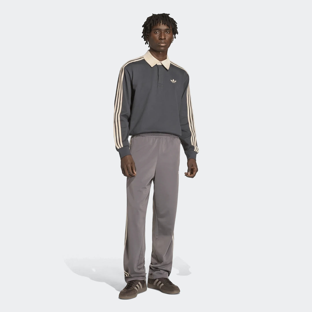 Male model in dark gray Adidas long-sleeve polo shirt, grey Firebird Track Pants with beige stripes, and brown sneakers.