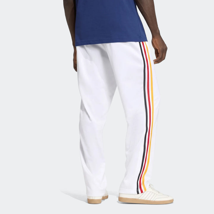 White Firebird Track Pants for men, featuring red, yellow, and black stripes on the side, worn by a model in an angled rear