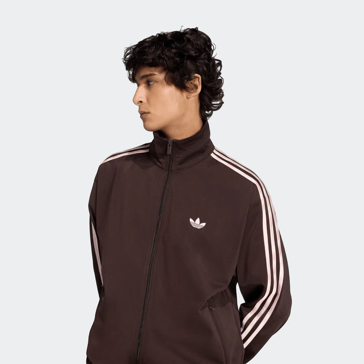 Men's brown Adidas Firebird Track Top with white three stripes on sleeves, worn by a model in a chest-up shot.