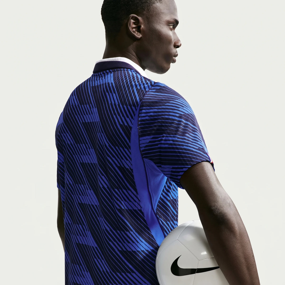 A dark-skinned man in a blue and black patterned Nike France National Team 2026 Match Home soccer jersey holds a white Nike
