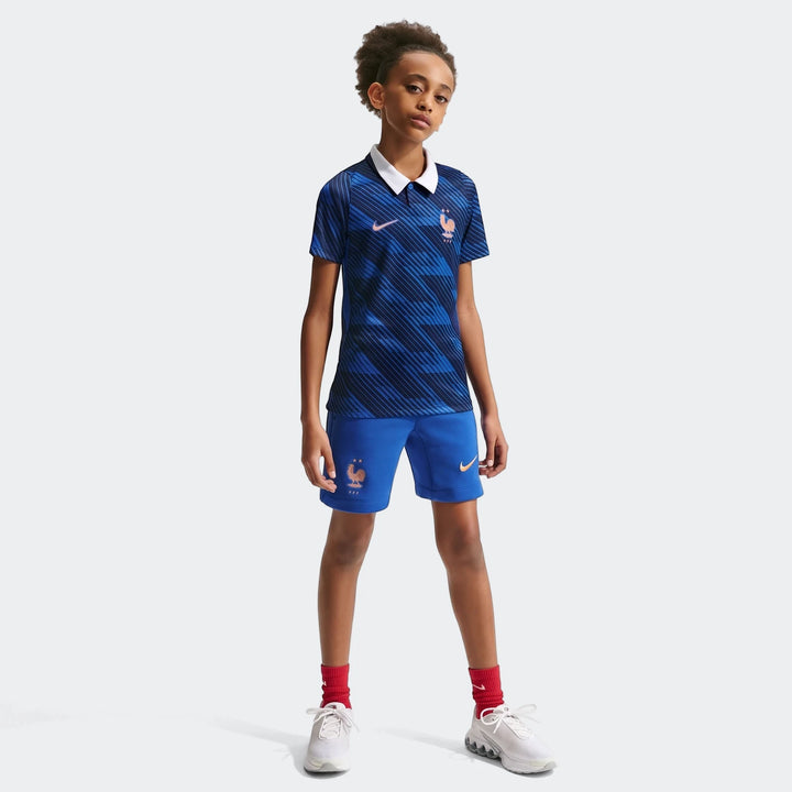 Young boy wearing the France National Team 2026 Stadium Home Blue Big Kids' Nike Dri-Fit Soccer Jersey, shorts, and red