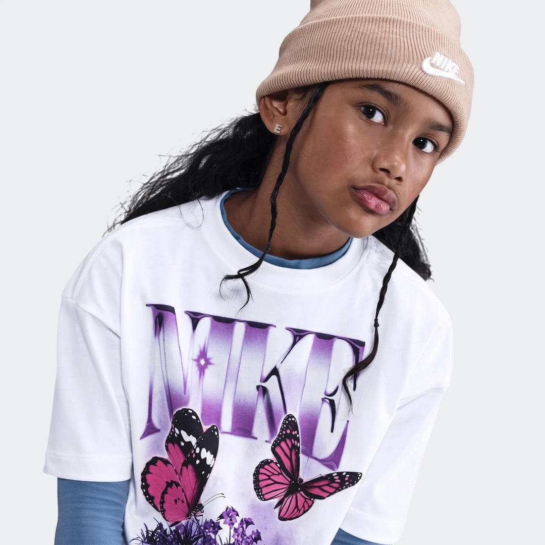 Young person wearing a white Nike butterfly t-shirt, beige Nike beanie, and blue undershirt, close-up shot.