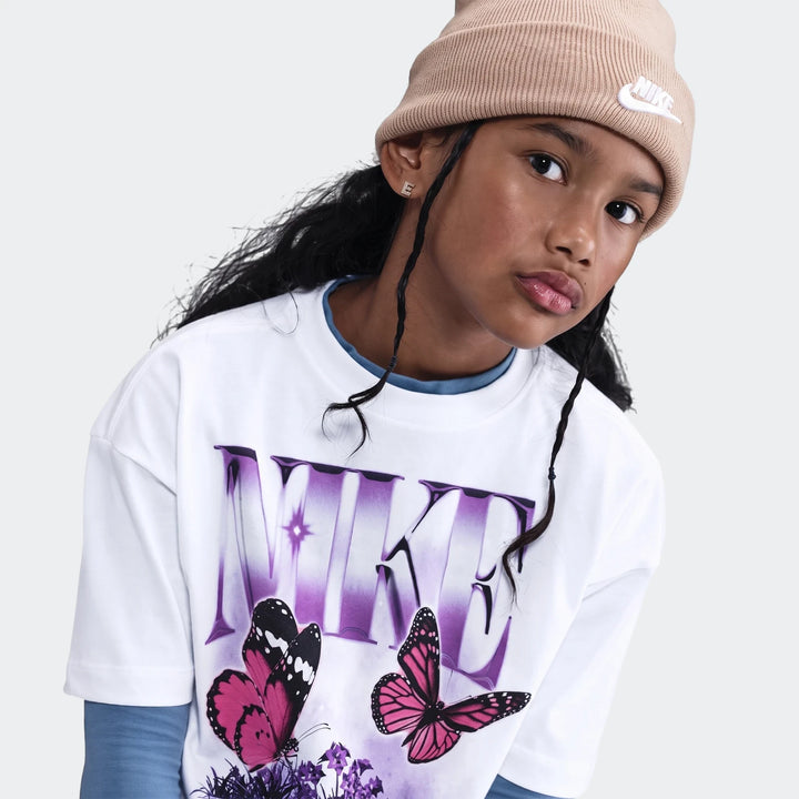 Young person wearing a white Nike butterfly t-shirt, beige Nike beanie, and blue undershirt, close-up shot.