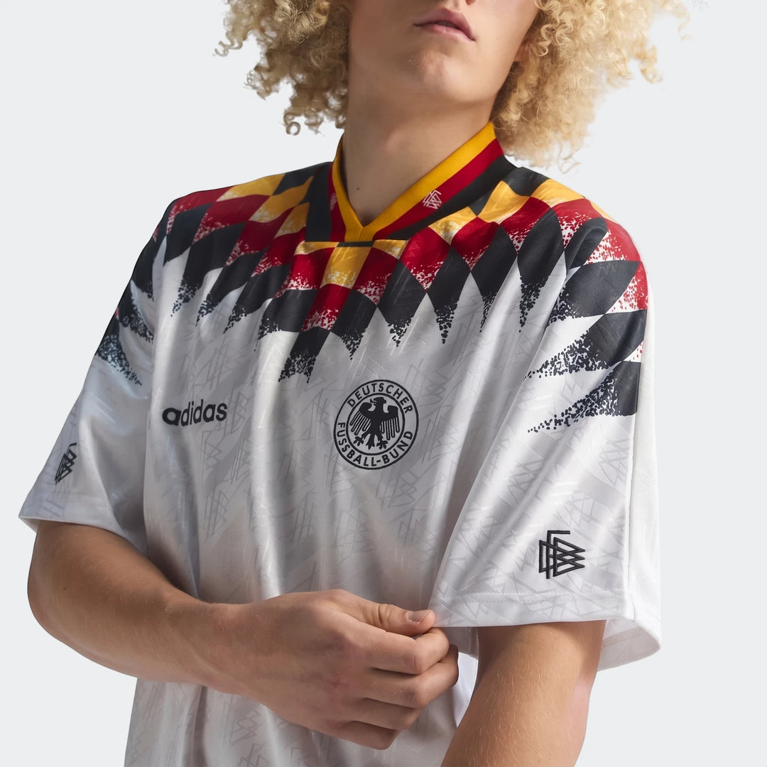Person wearing a white, black, red, and yellow Germany 1994 Retro Home Jersey with a distinctive diamond pattern.