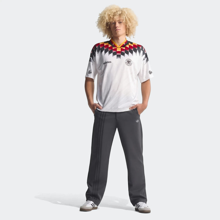 Full body shot of a male model wearing the white Germany 1994 Retro Home Jersey, paired with dark grey Adidas track pants