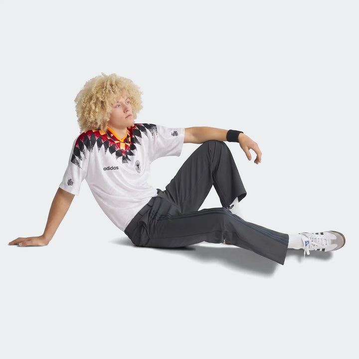 Germany 1994 Retro Home Jersey in white with black, red, and yellow diamond pattern, worn by a model sitting on steps, full
