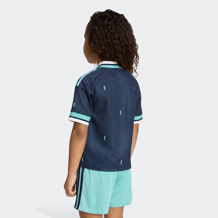 Child wearing Germany 25/26 Away Mini Kit, featuring a dark blue jersey with a patterned design and light blue shorts,