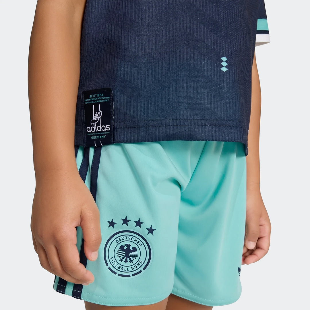 Close-up of a child wearing the Germany 25/26 Away Mini Kit, featuring a dark blue jersey and light blue shorts.