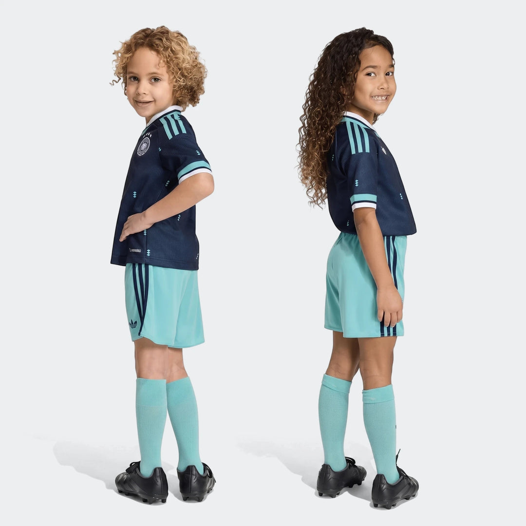 Two young children wearing Germany 25/26 Away Mini Kit in navy blue and teal, including jersey, shorts, and socks, full body