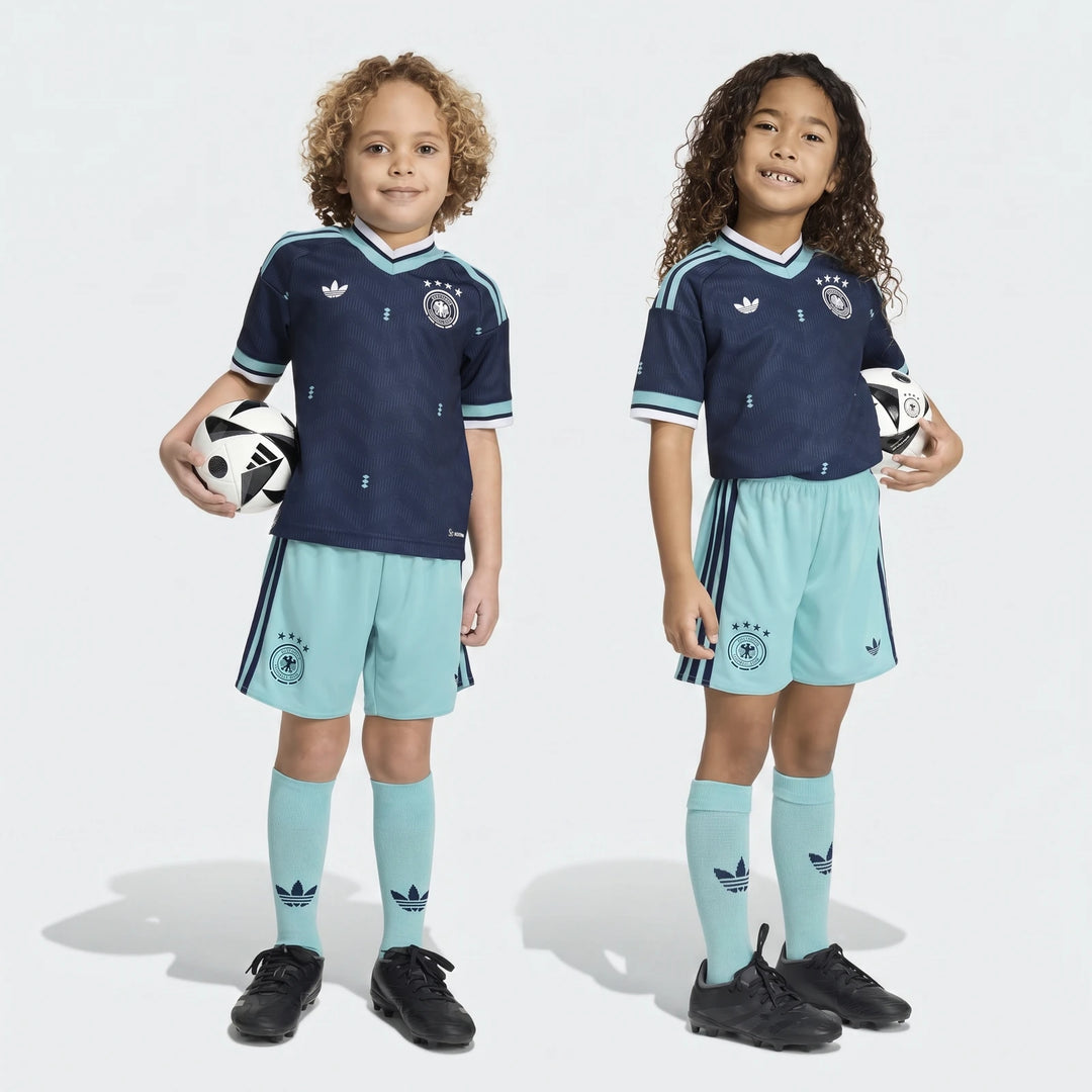 Two young children wearing the Germany 25/26 Away Mini Kit, featuring a navy blue jersey and light blue shorts, holding