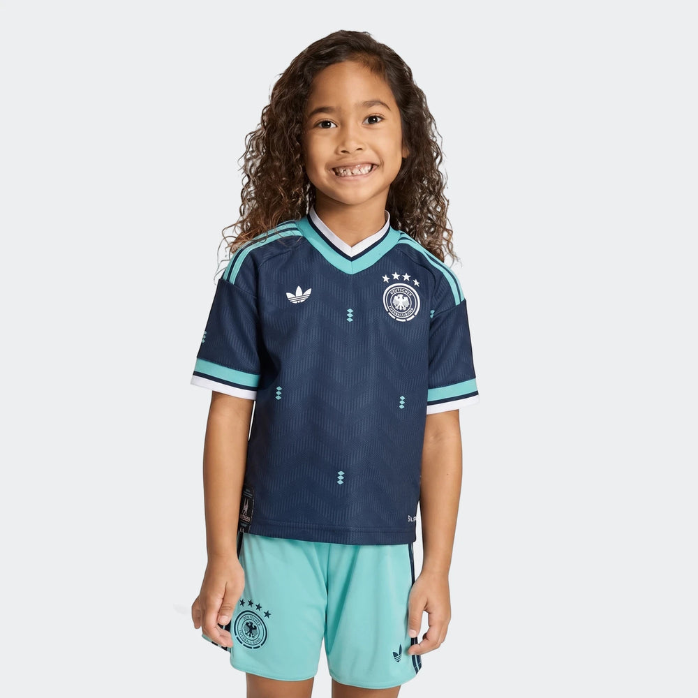 Young girl smiles wearing Germany 25/26 Away Mini Kit, featuring navy blue jersey with light blue details and matching