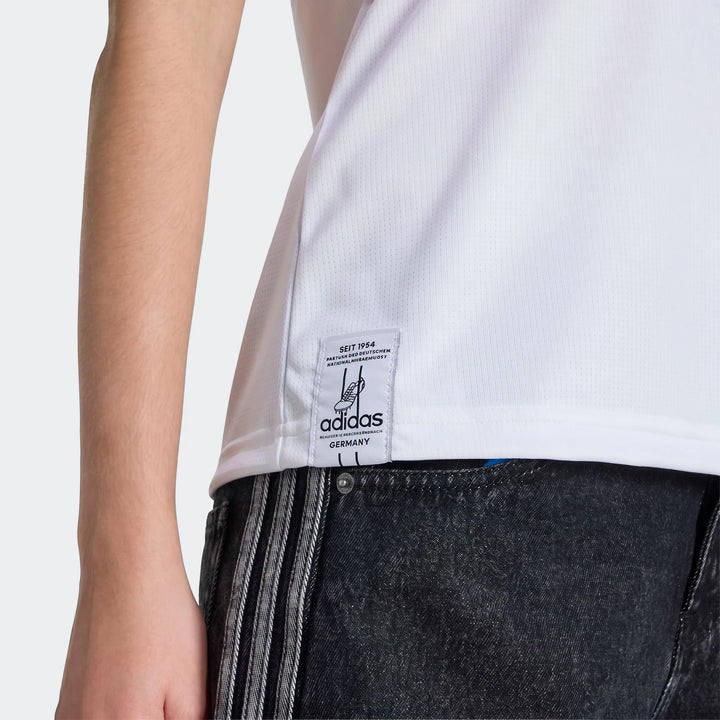 Close-up of a white Adidas Germany 25/26 Home Jersey for women, featuring the brand label, worn with dark jeans.
