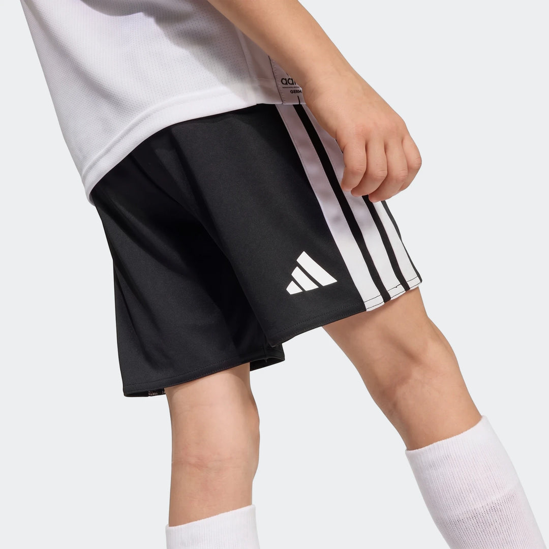 Close-up of a child wearing the Germany 25/26 Home Mini Kit, featuring black shorts with white stripes and logo, a white