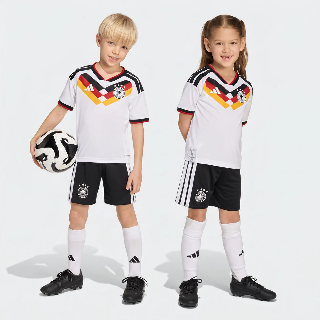 Germany 25/26 Home Mini Kit for kids, featuring white jersey, black shorts, and socks, modeled by a boy and a girl.