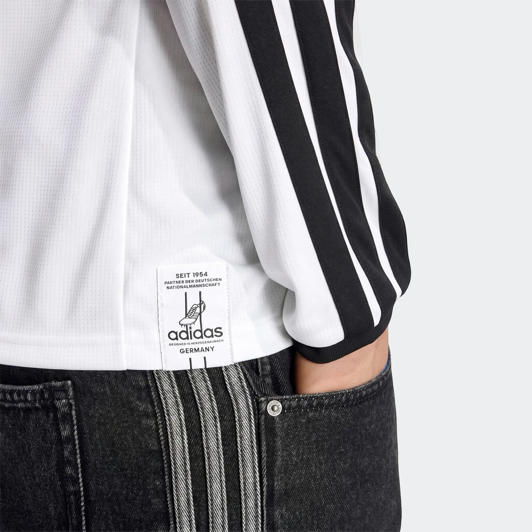 White Adidas Germany 25/26 Long Sleeve Home Jersey with black stripes, worn by a person paired with dark gray jeans.