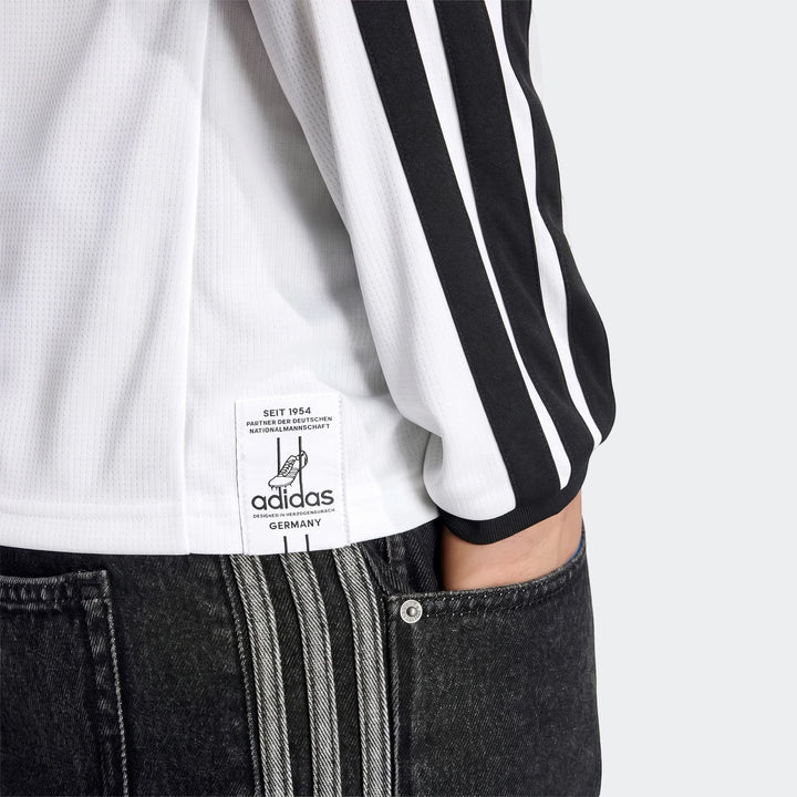 White Adidas Germany 25/26 Long Sleeve Home Jersey with black stripes, worn by a person paired with dark gray jeans.