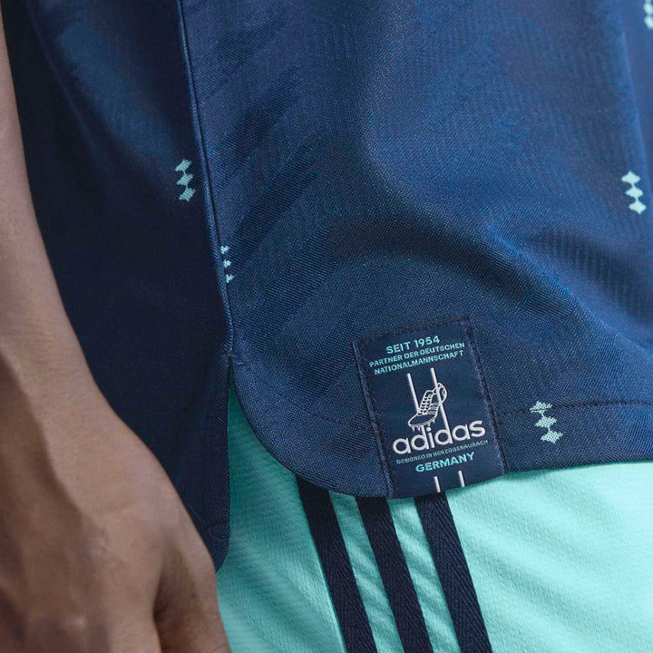 A close-up of the dark blue Germany 26 Away Authentic Jersey with a detailed Adidas tag and light blue striped shorts