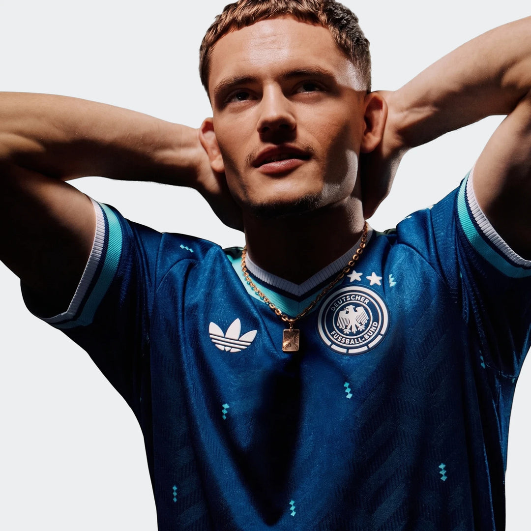 Male model wearing a dark blue Adidas Germany 26 Away Authentic Jersey with a gold chain, looking up.